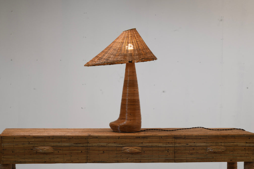 Illuminated Chloe rattan table lamp with an asymmetric woven shade and curved wrapped base on a three-drawer rattan console.