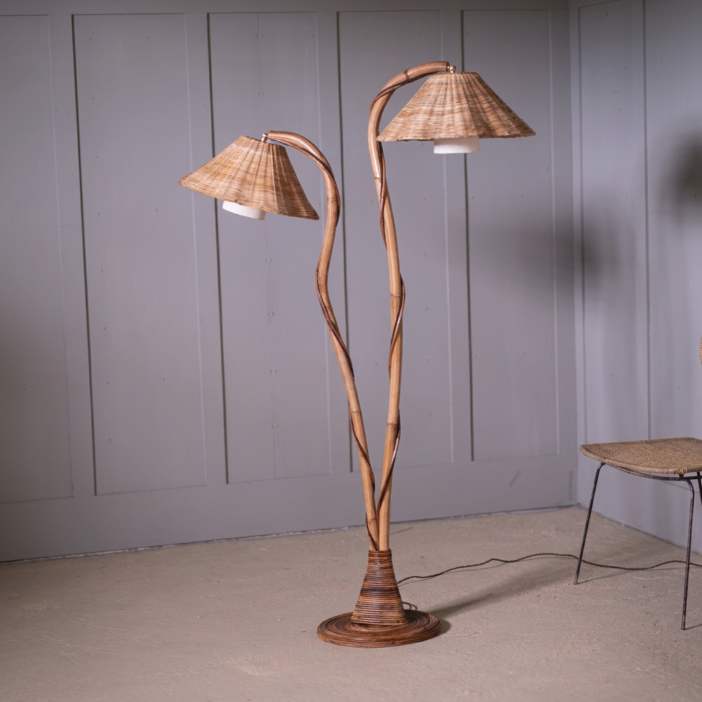 Thalia twin-stem rattan floor lamp with two woven shades and a round base against a grey panelled wall.